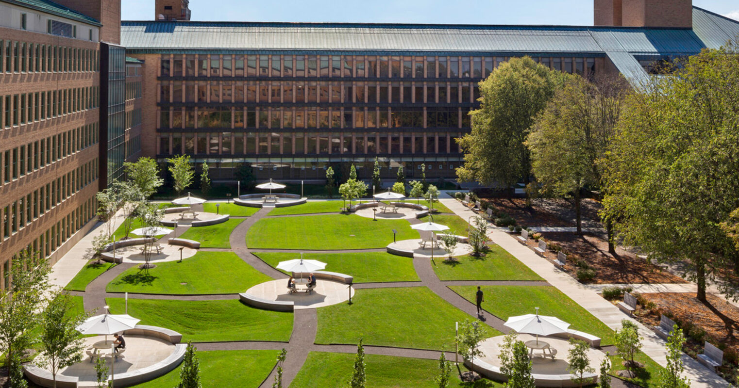 An urban oasis: verdant gardens and circular seating areas offer a peaceful retreat amidst modern brick buildings.